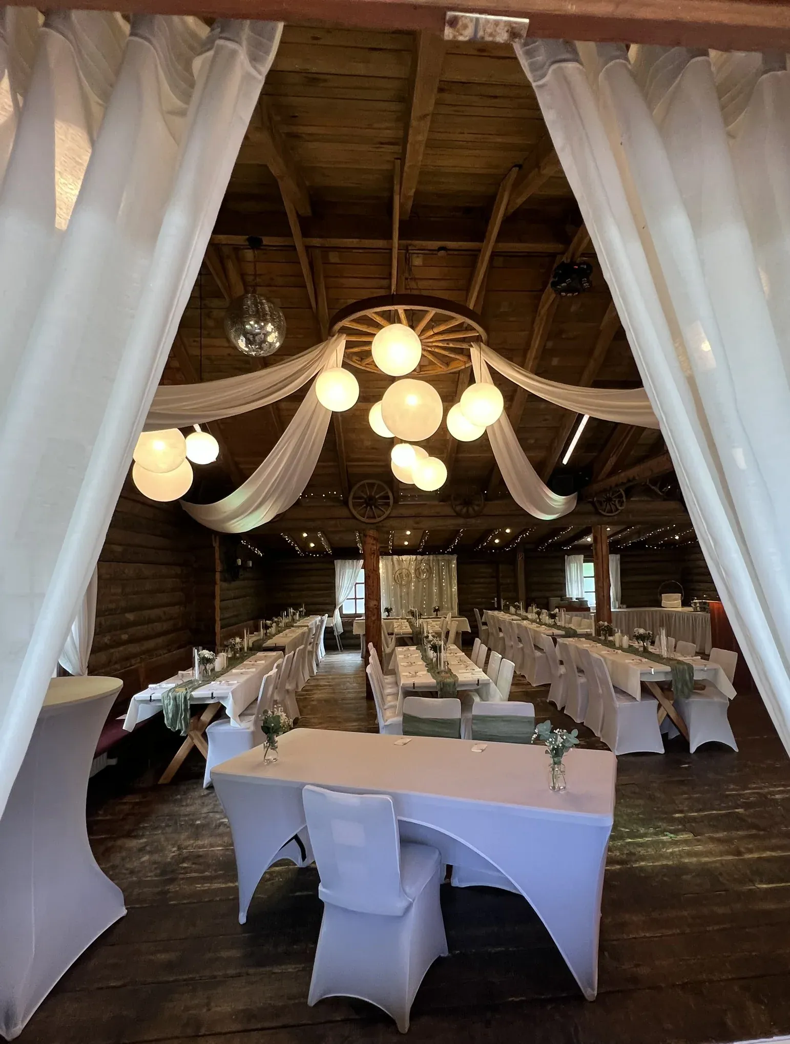 Blick durch weiße Vorhänge in den Festsaal mit Lampions und gedeckten Tafeln