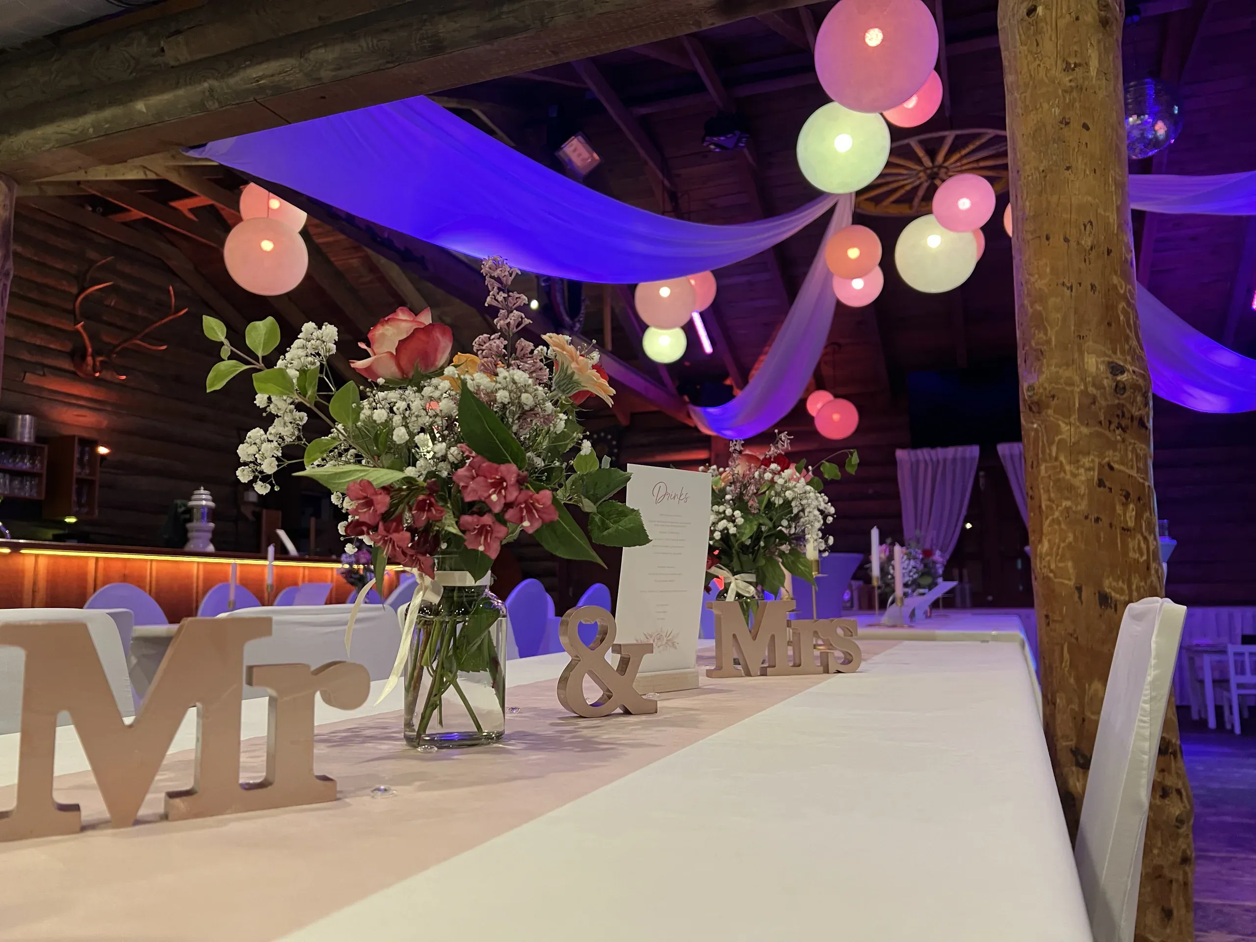 Brauttisch mit Blumenstrauß und Holzbuchstaben, darüber bunte Lampions